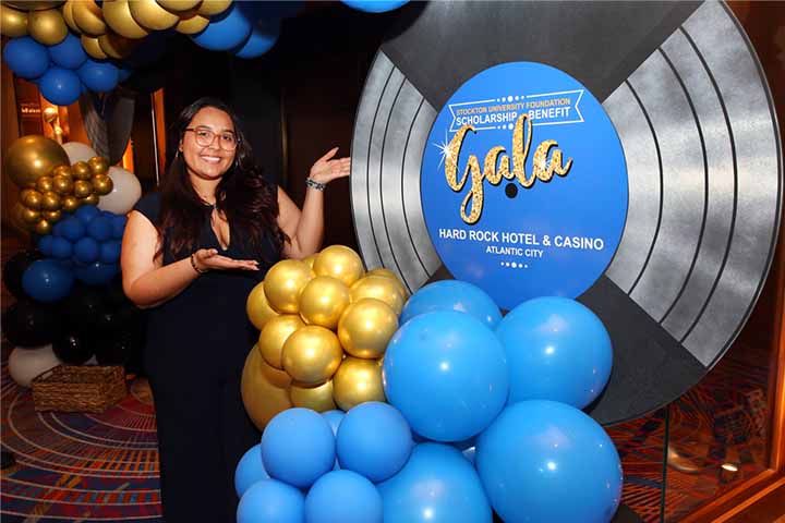 Alumna next to balloon column with Scholarship Benefit Gala sign