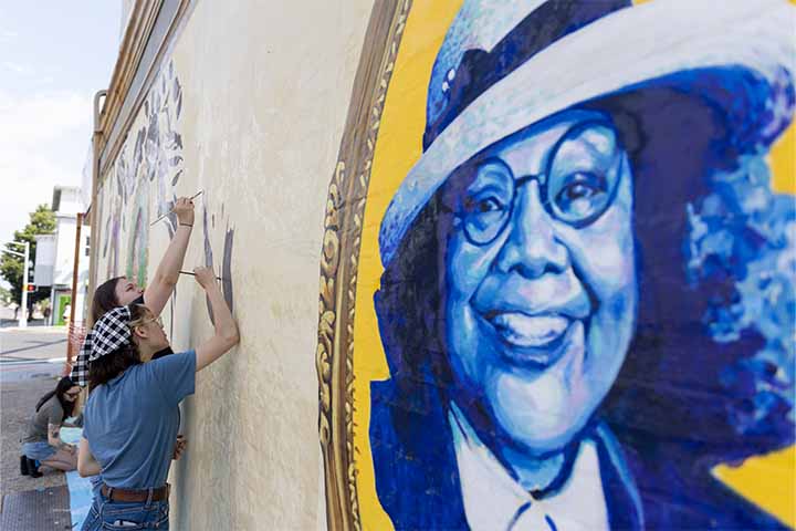 Students painting on wall next to blue and yellow mural of Vera King Farris
