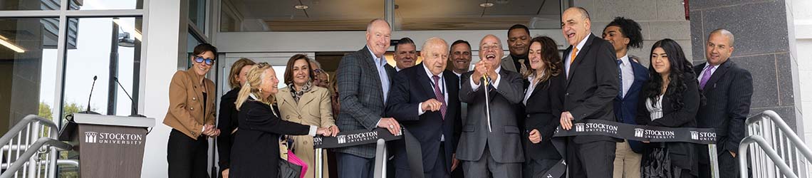 A group of university leaders cut a black ribbon to open a new building