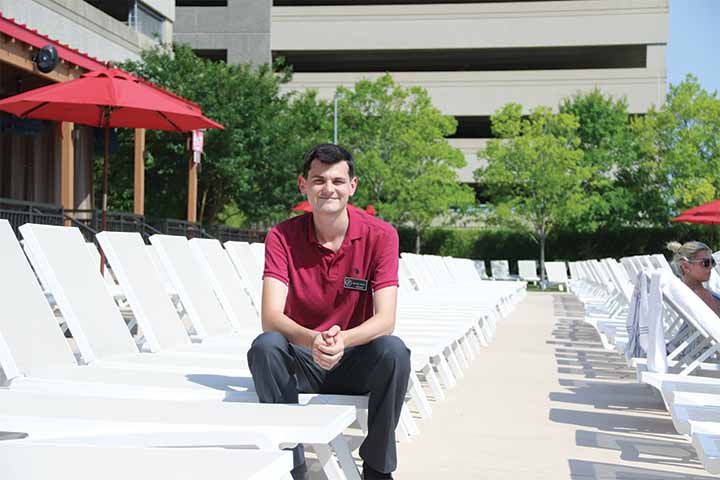 A student in red polo shirt sits on a lounge chair on an outdoor patio