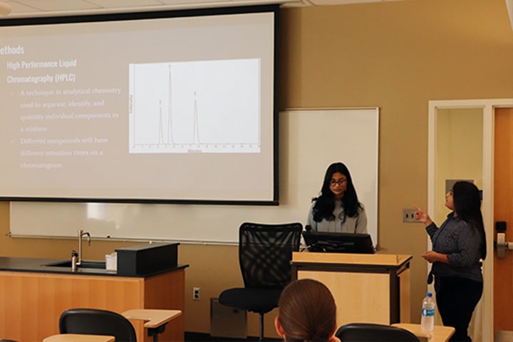 Two students presenting at a podium in front of a classroom