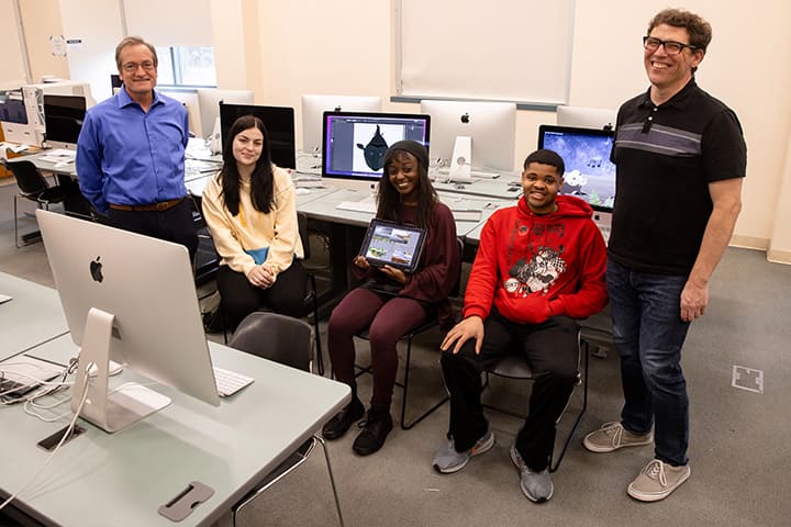 Two standing faculty members and three sitting students in a computer lab