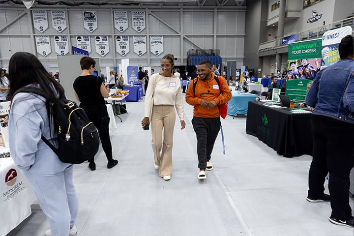 Two students walk through a gymnasium lined with tabling employers