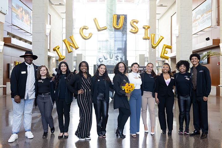 A group of students and administrators in front of a balloon arch spelling out Inclusive