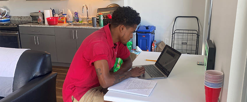 A student in red polo shirt working on a laptop at a table