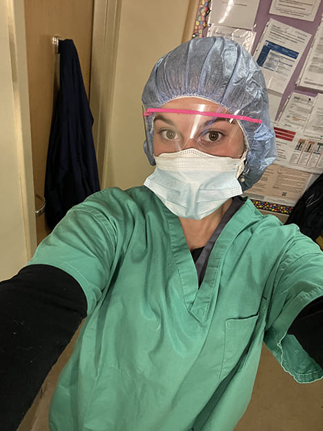 A nursing student in green scrubs, hair net, face mask and shield