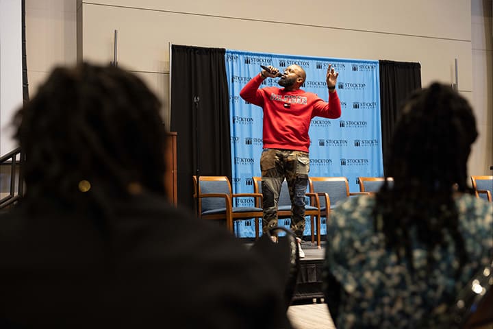 A man in a red sweatshirt speaks passionately into a microphone