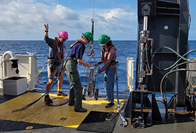 Three people in hard hats working on the deck of boat at sea