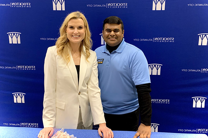 Joy Jones and Rifat Mahmud stand together in front of a royal blue step-and-repeat banner with the Stockton logo