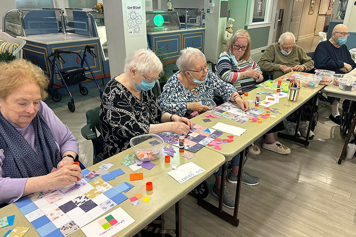 A group of older individuals sit at a table working on an art project