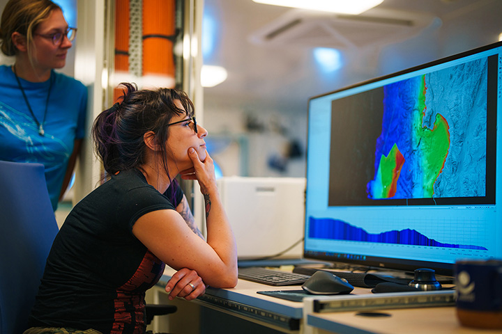 Lauren Seyler sits at a desk and looks at sonar imaging on a computer screen