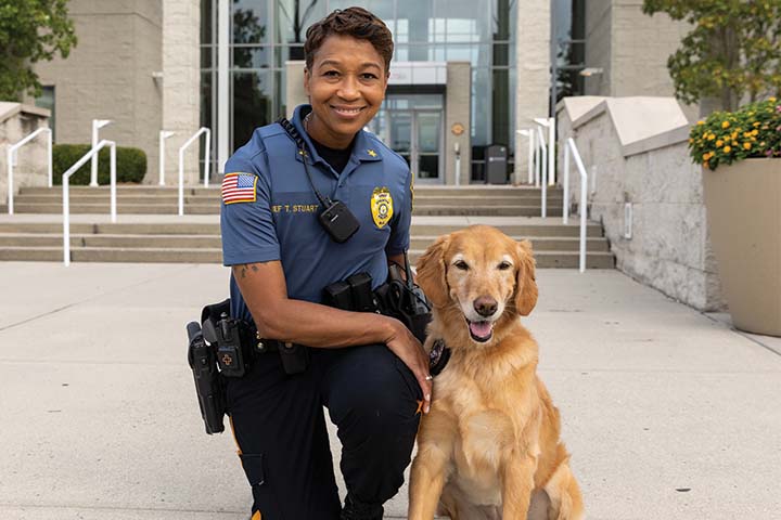 Chief Tracy Stuart in police uniform kneeling next to golden retriever K-9 Freya in front of the Campus Center