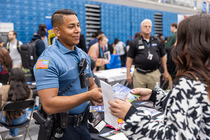 A police officer in uniform hands a pamphlet to an interested student inside Stockton's Sports Center