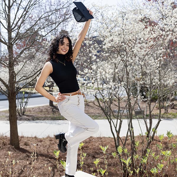 Ashley Rivera in front of the Campus Center, holding her graduation cap over her head