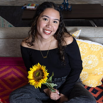 Britney Marrugo sitting in the Multicultural Center, holding a sunflower