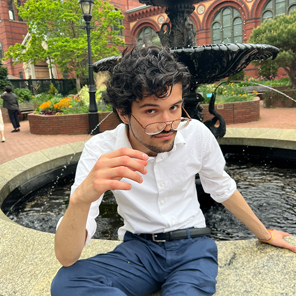Esteban Agudelo, sitting on a fountain with his glasses perched on his nose
