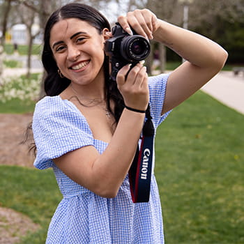 Joselyn Riess smiling and holding up her camera, taking a photo of our photographer 