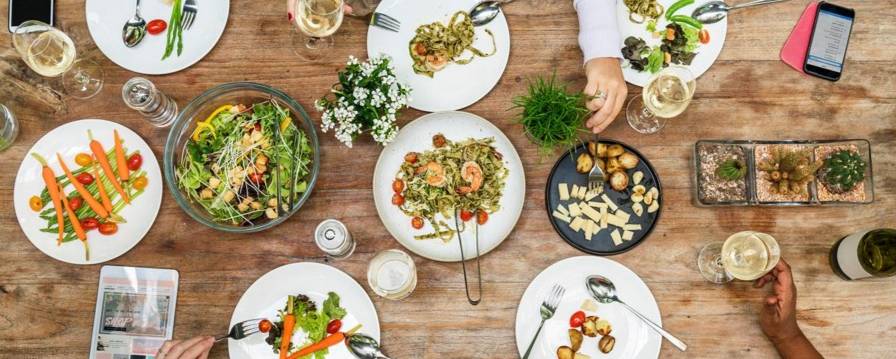 Overview shot of plates of food on a dining table and people eating.
