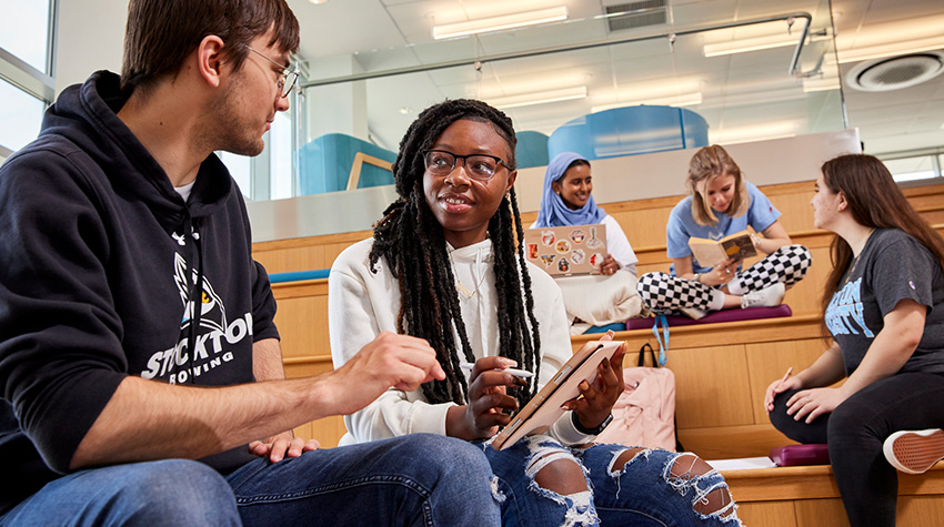 Students on the Stair Lounge in Atlantic City; two are talking about something on an iPad and three are behind them, talking to each other and reading