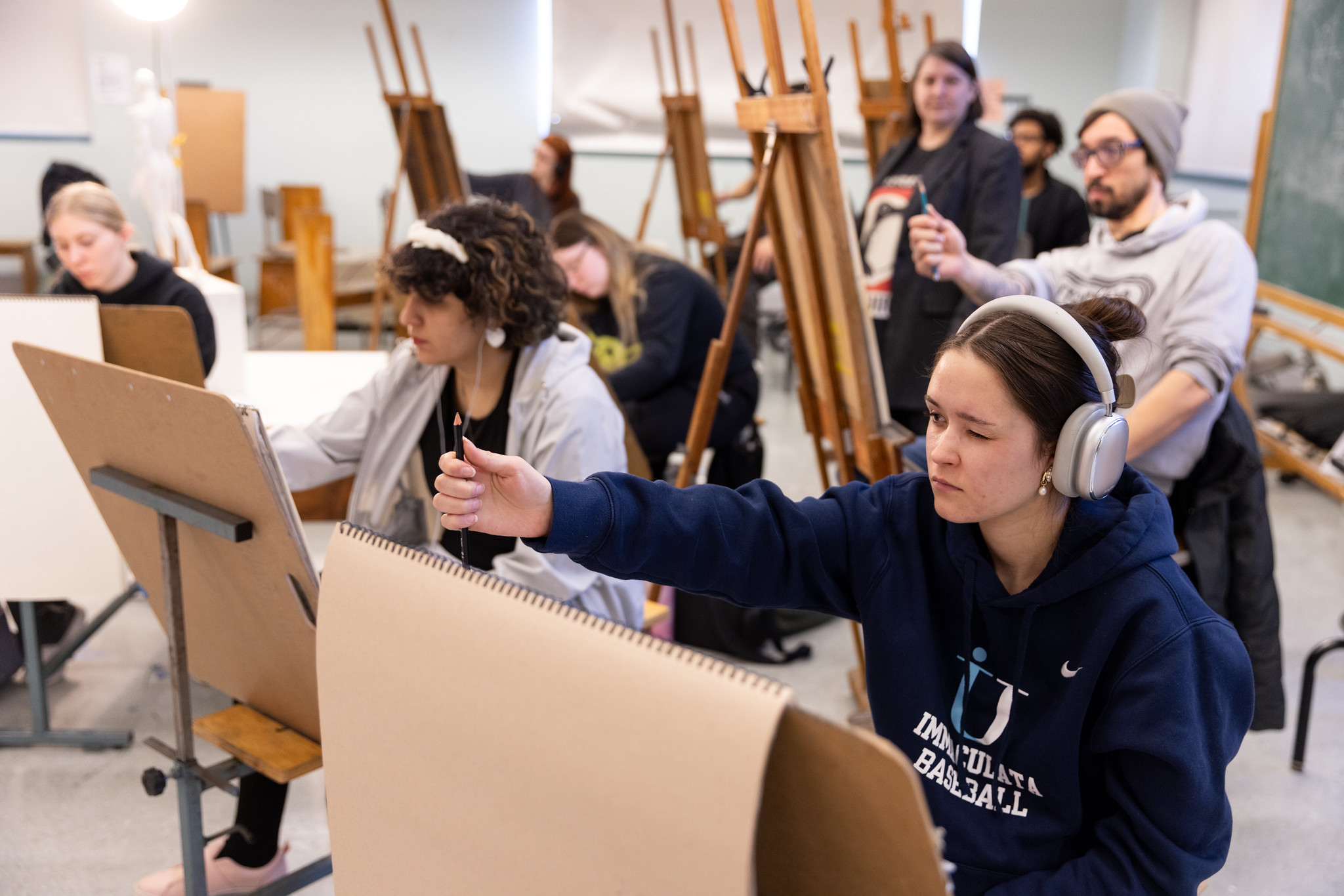 Students with easels and drawing pads holding pencils to determine the scale of a drawing.