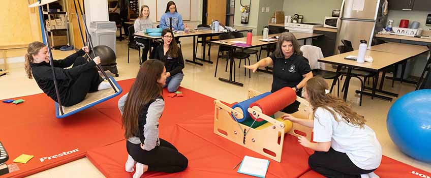 A faculty member and six students work with occupational therapy equipment