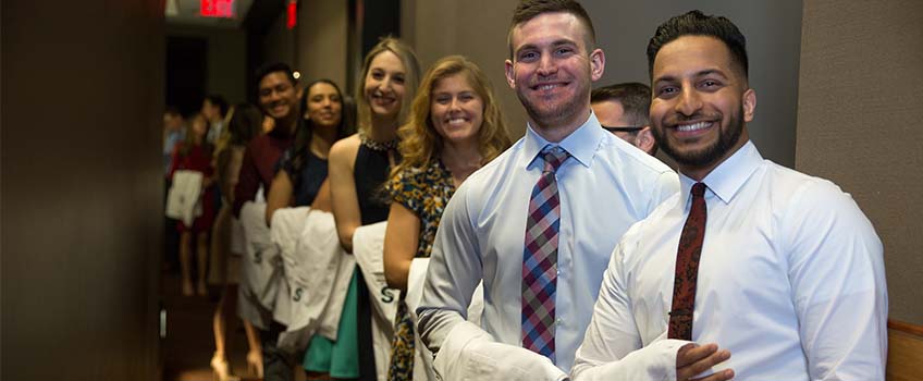 Physical Therapy students smile with their white coats over their arms