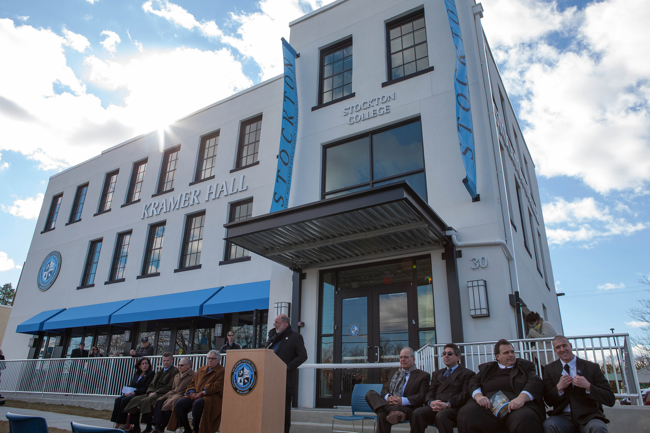 Man speaking at podium with people on either side of him for the grand opening of Kramer Hall