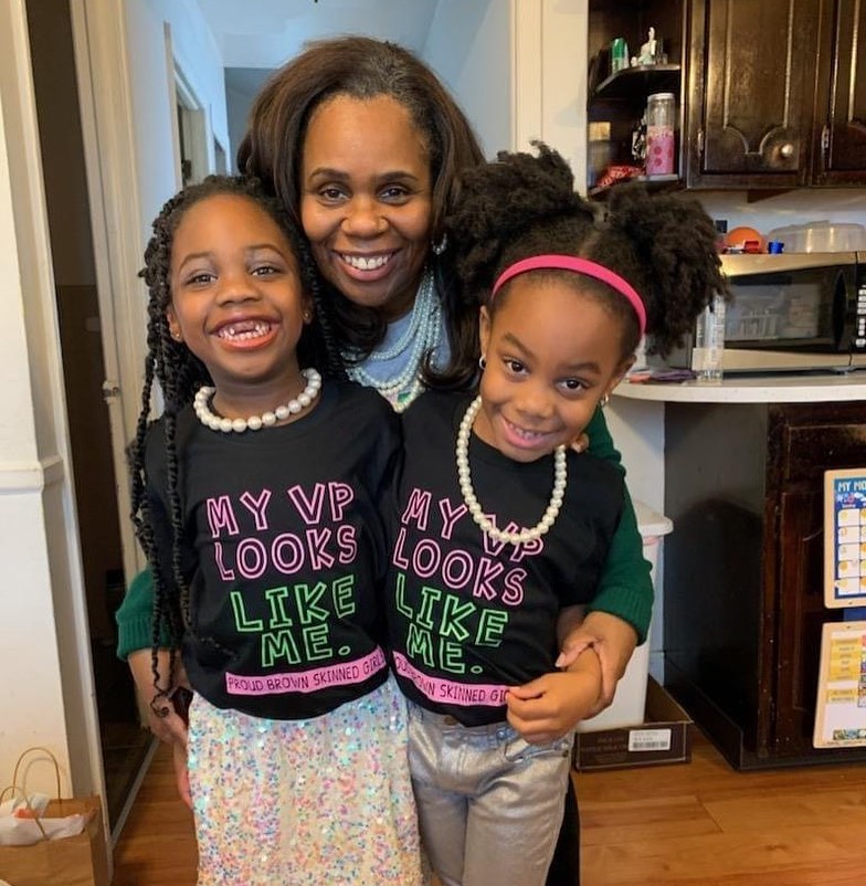 Maya Lewis with her twin daughters, who are wearing t-shirts that say "My VP looks like me!"