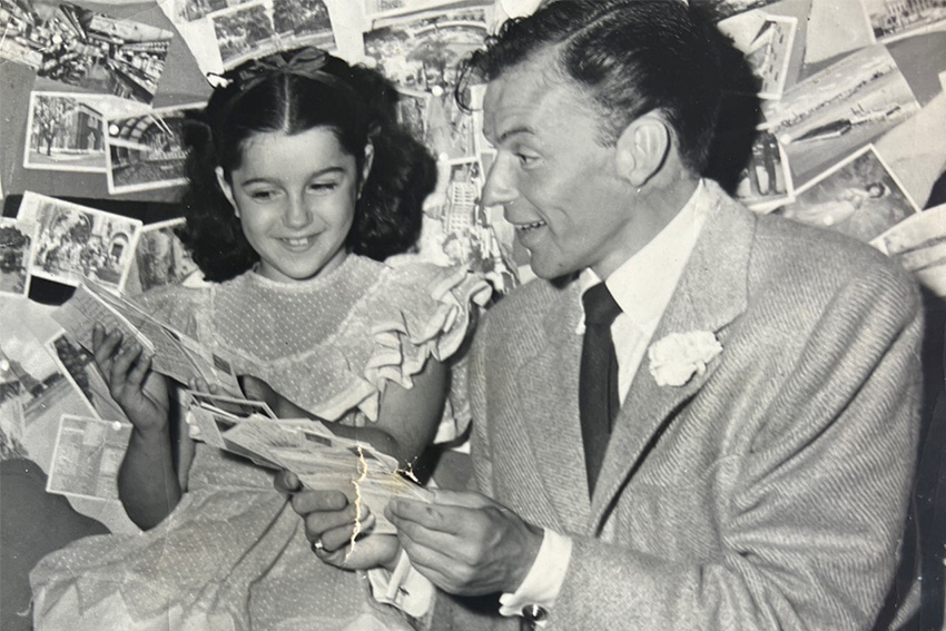 Vicki Gold-Levi as a child with Frank Sinatra. They're sitting together and shes showing him a book.