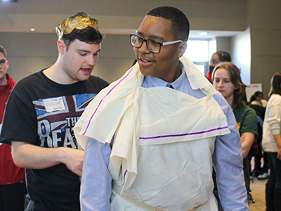 A student getting his toga tied by a Stockton student