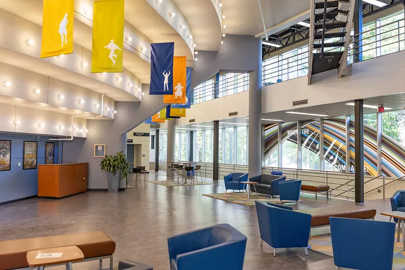 Bright modern atrium with colorful banners, lounge seating, large windows, and a staircase.