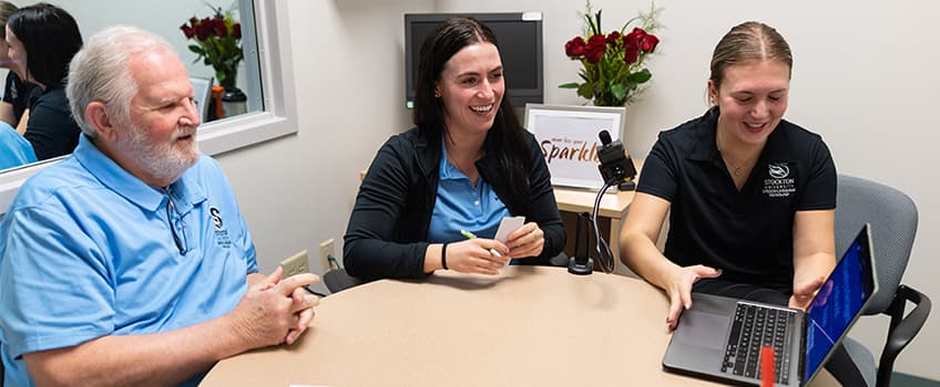 Man and two women sit around table with laptop
