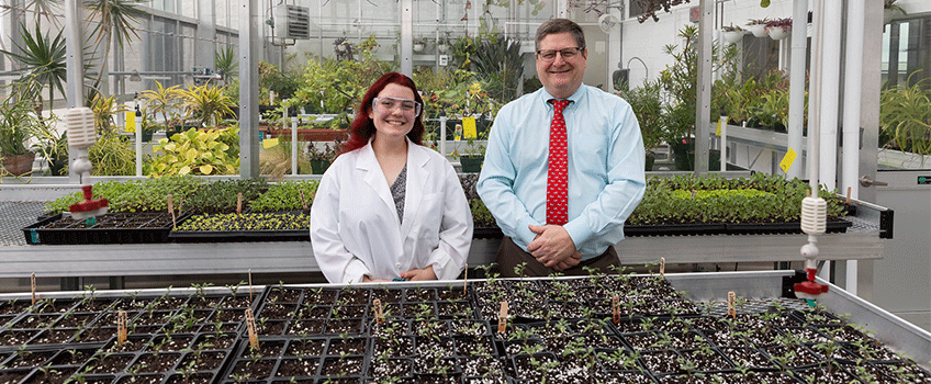 female student and man standing in greenhouse 