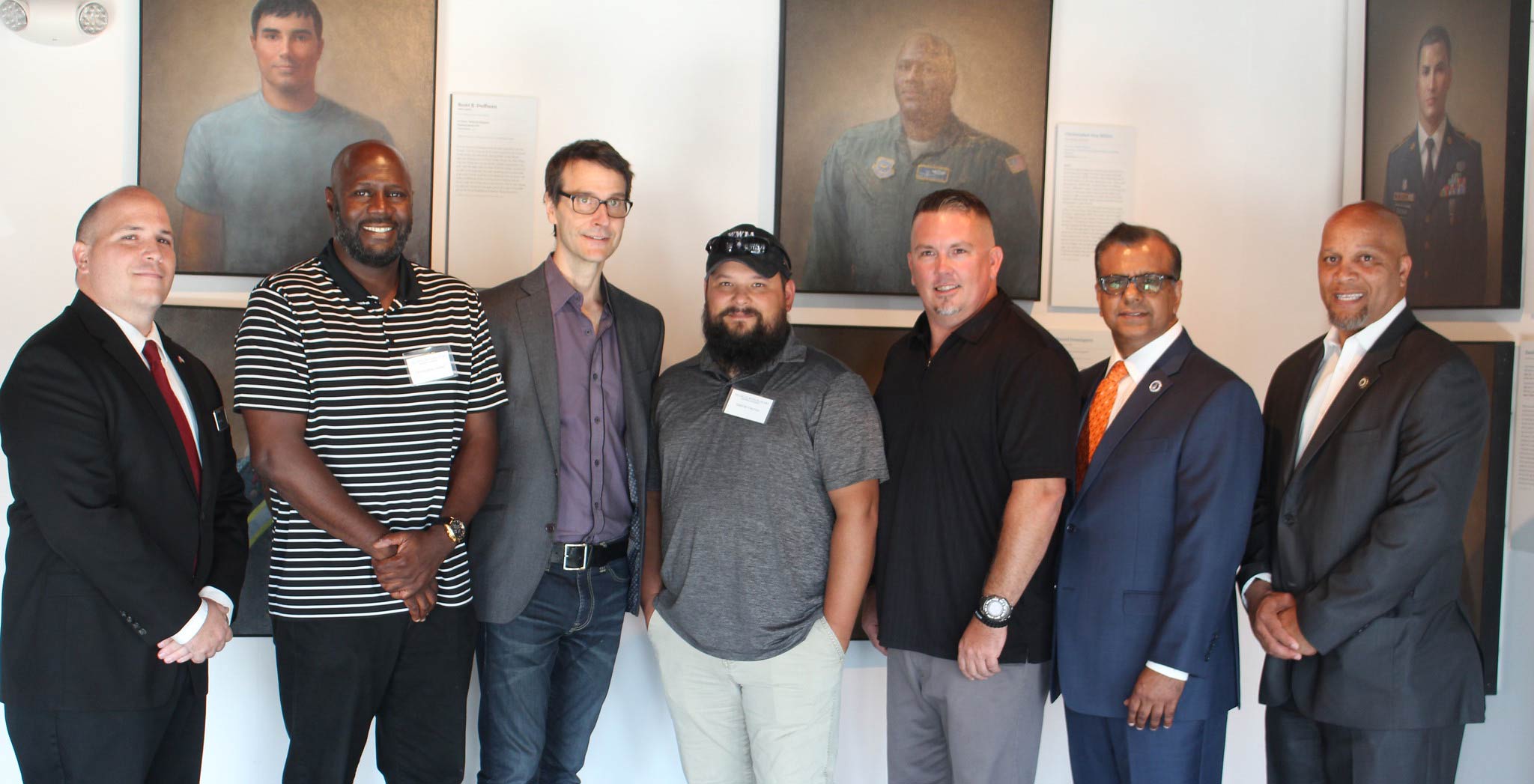 seven men standing in front of portraits