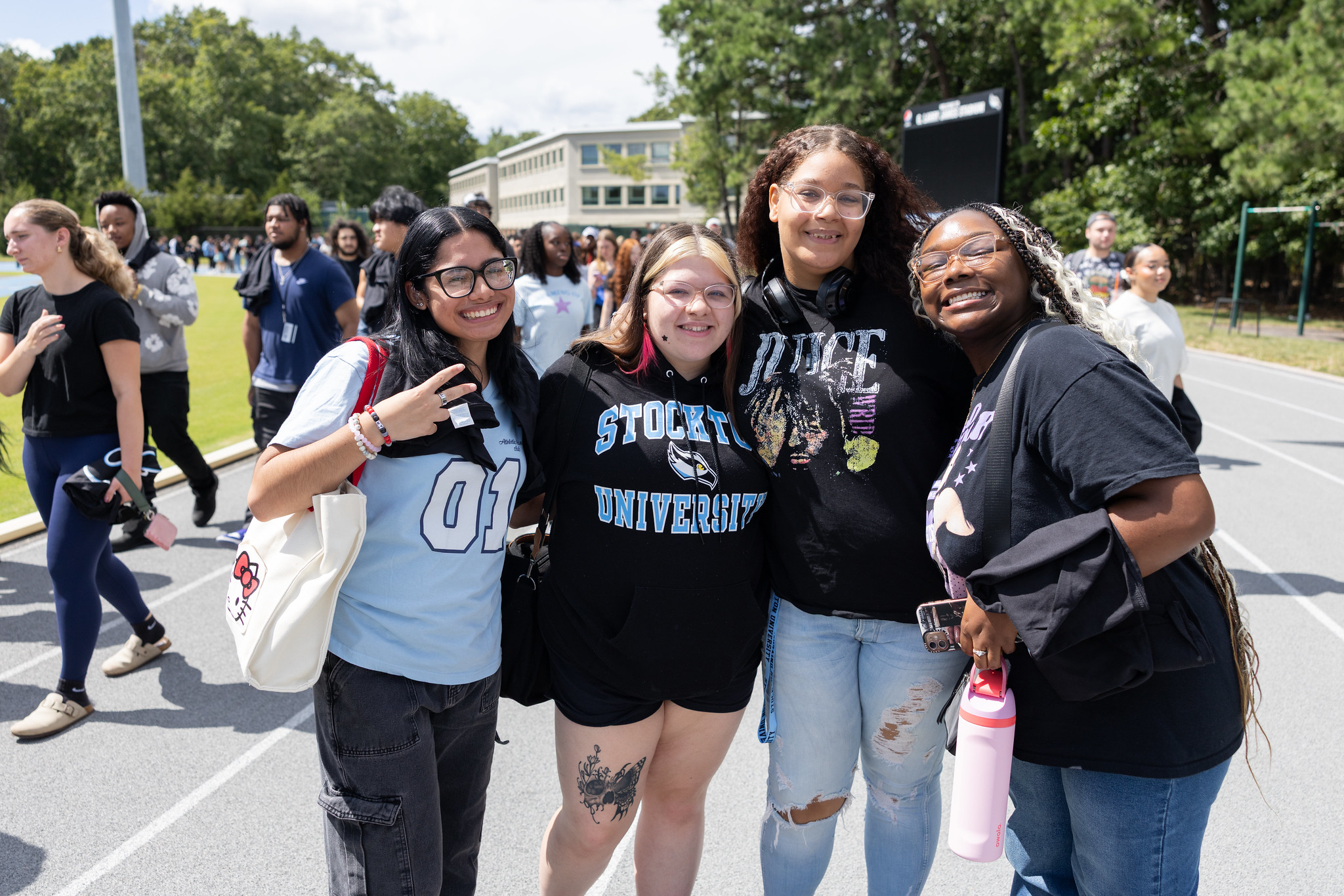Four new students smile together outdoors during campus event, wearing casual clothes and Stockton University apparel.