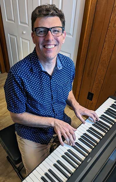 Matt Bonnan in a blue short sleeve button behind a piano keyboard