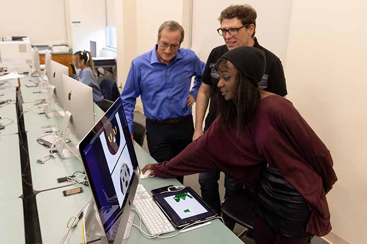 A college student shows off her work on a computer screen to two professors