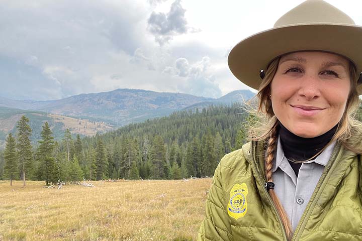 Kimberly Dudeck wearing a park ranger's hat and green jacket in an open field