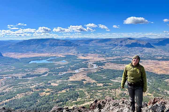 Kimberly Dudeck stands near the edge of a cliff overlooking green and brown open land