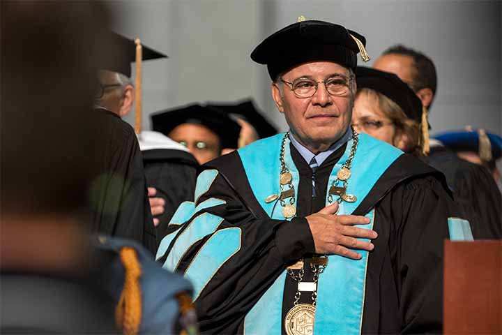 Harvey Kesselman in commencement regalia with his hand over his heart