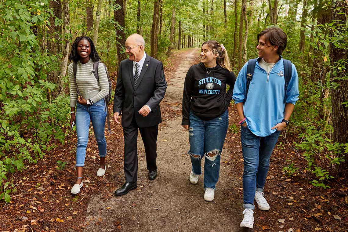 Harvey Kesselman walks with three students along a wooded, natural path