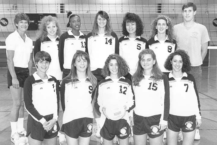 A black and white photo of 10 volleyball players and two coaches in a gym