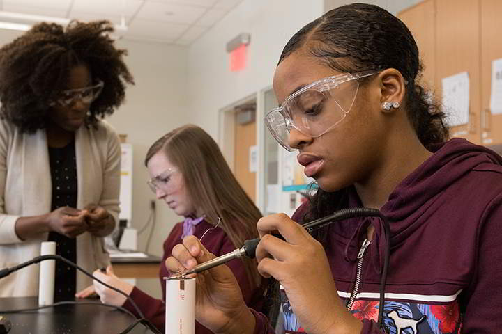 Nephthaly Jean-Charles ’16 (far left) assists two middle school students  as they solder underwater flashlights during Tween Tech at Stockton in January 2017