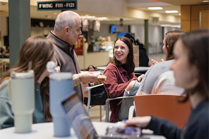 Joe Bertolino talks to students sitting at high top tables outside the library