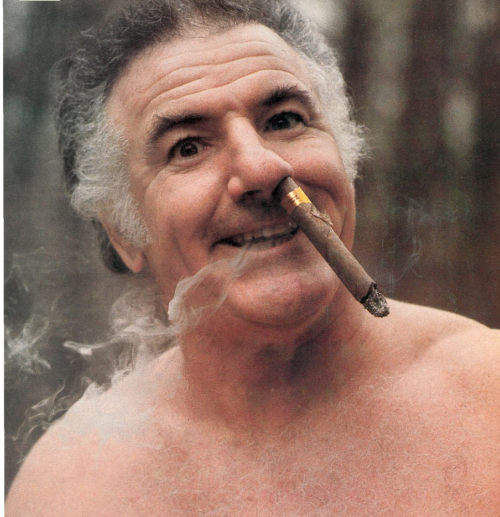Don Bragg shirtless with a cigar hanging out of a nostril
