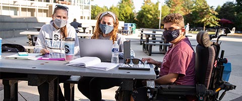 three students with laptops outside